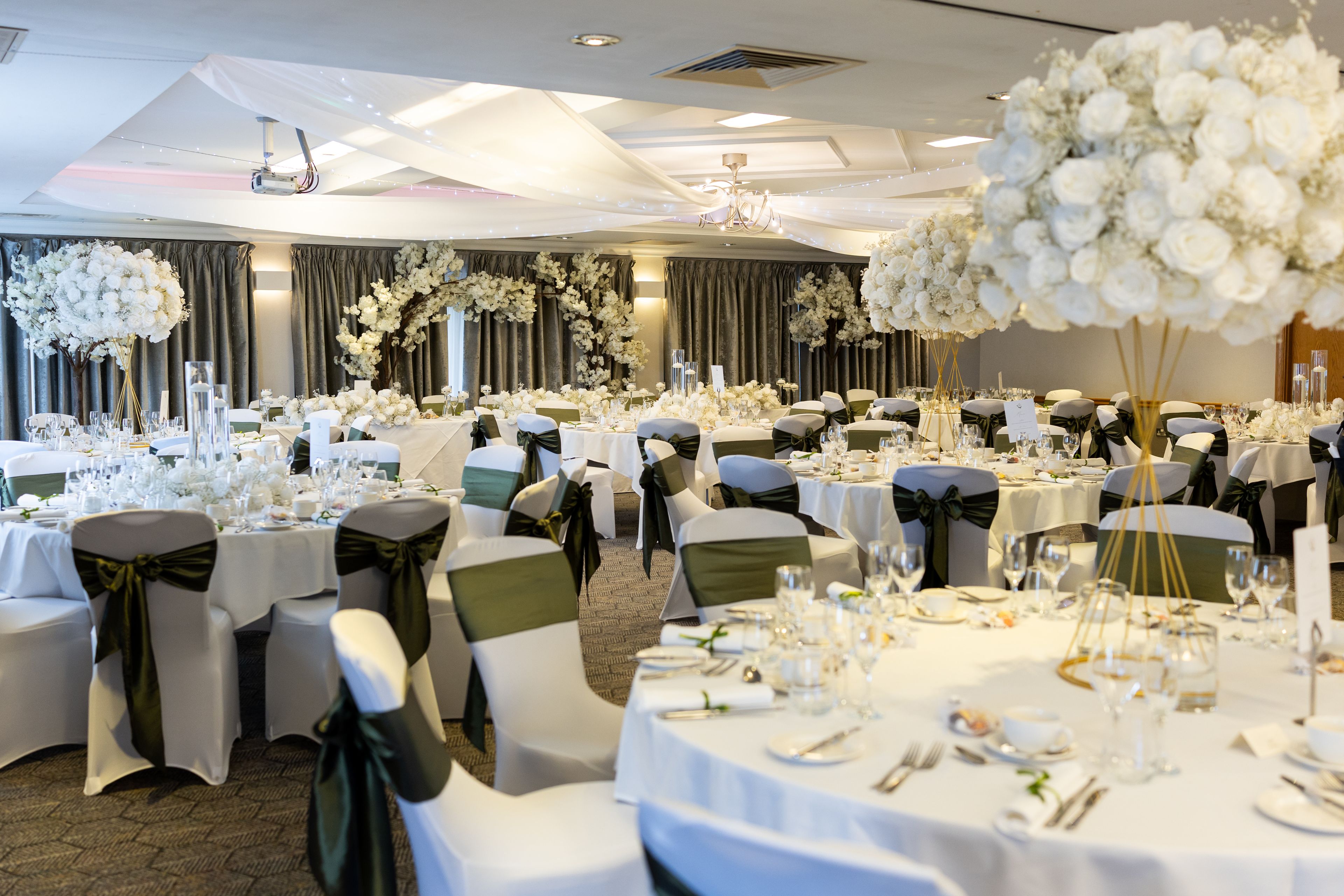 Room dressed with white table clothes and dark chair ribbons